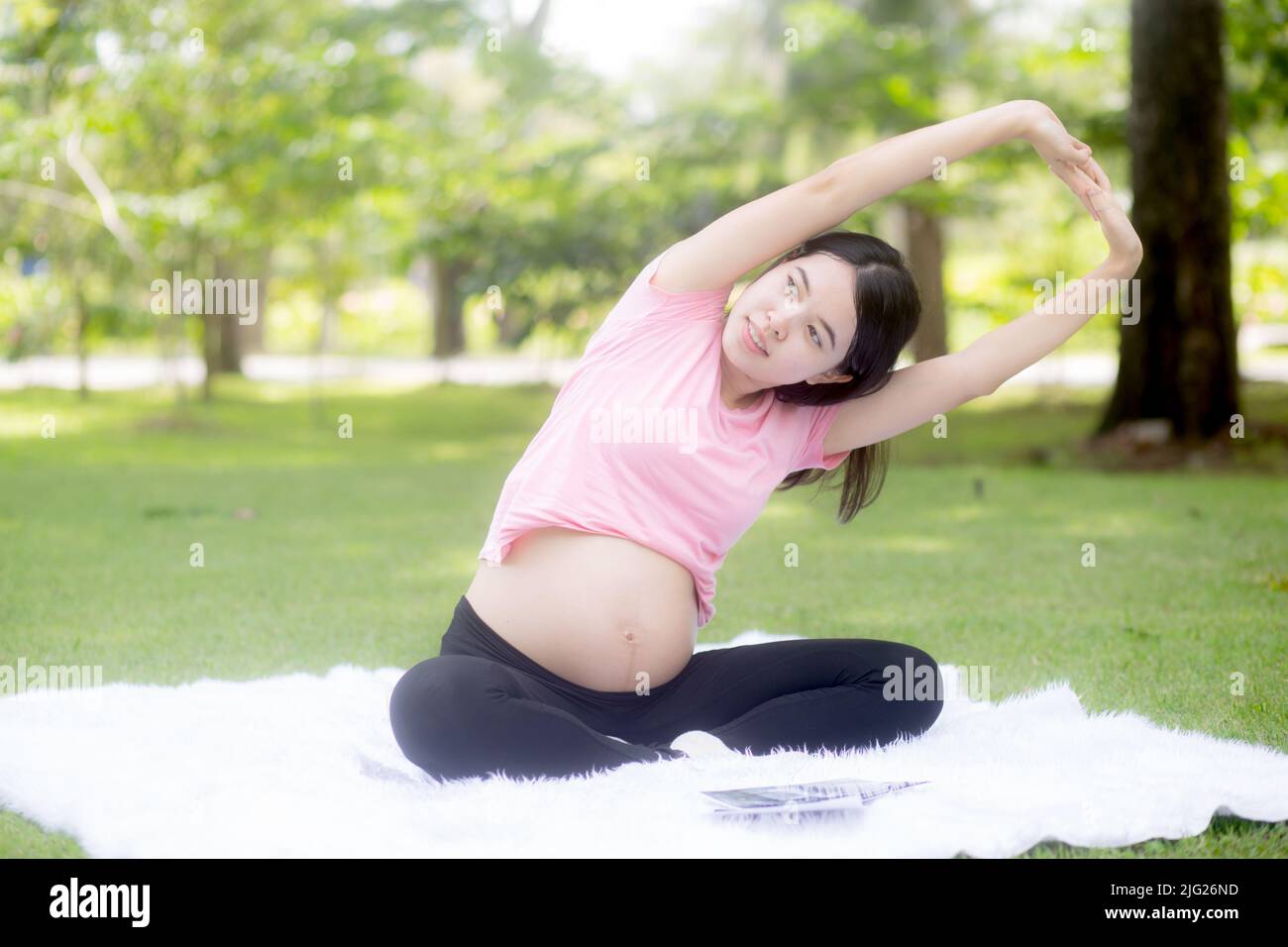 Felicità giovane donna asiatica incinta seduta facendo esercizio sportivo con mani stretch muscolo per la salute al parco, madre che pratica yoga per il leisur Foto Stock