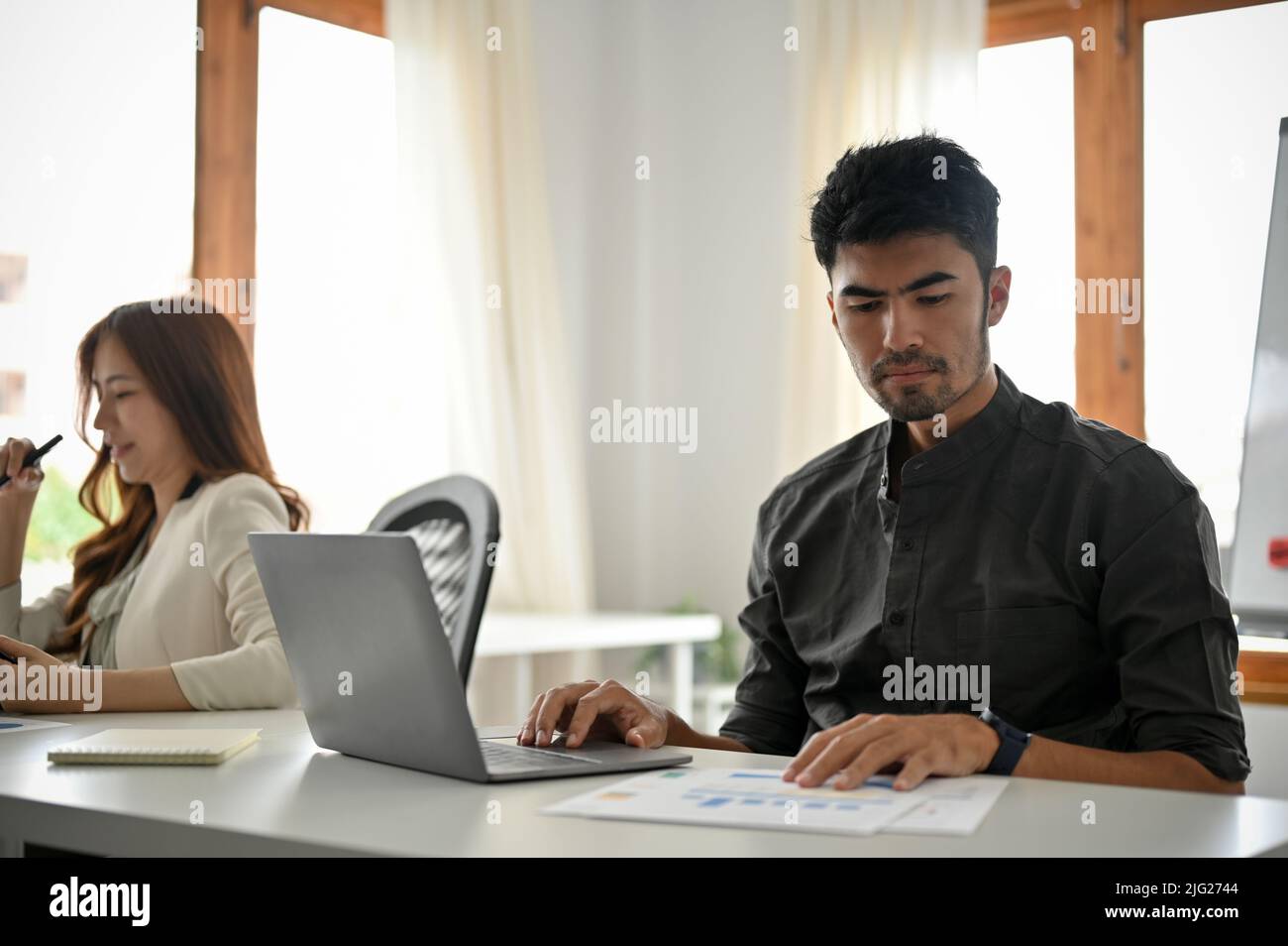 Bell'uomo d'affari asiatico giovane-adulto e intelligente si è concentrato a lavorare su un rapporto di dati finanziari e utilizzando il computer portatile in ufficio. Foto Stock