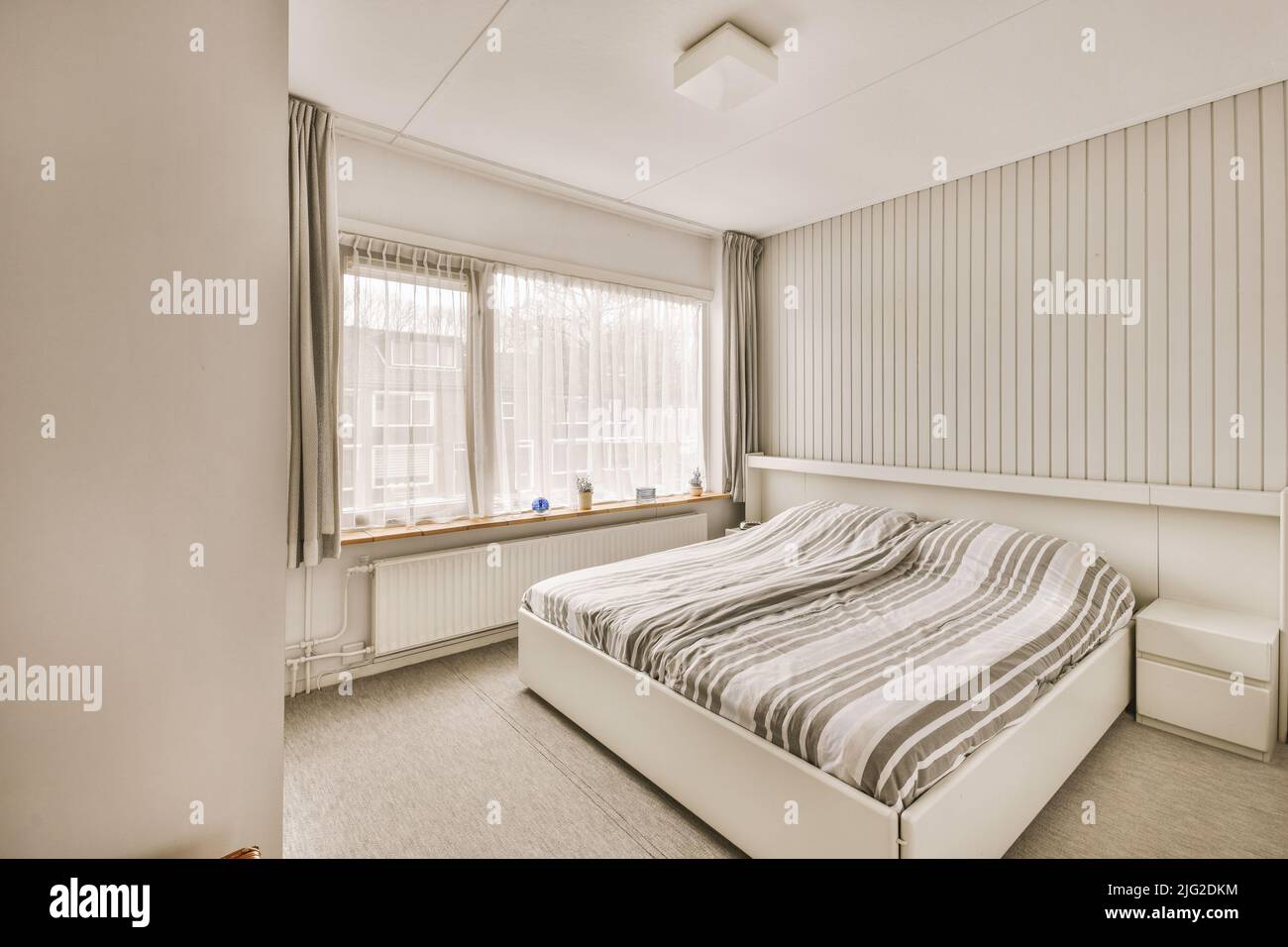 Letto moderno con comodo materasso situato vicino al pouf del comodino e guardaroba in una spaziosa camera da letto Foto Stock