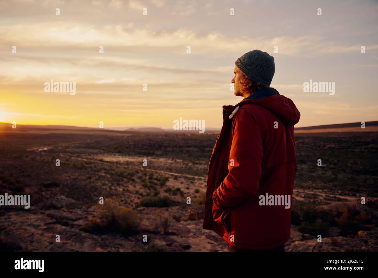 Uomo premuroso che indossa giacca e berretto in piedi sulla montagna guardando l'alba mattina Foto Stock