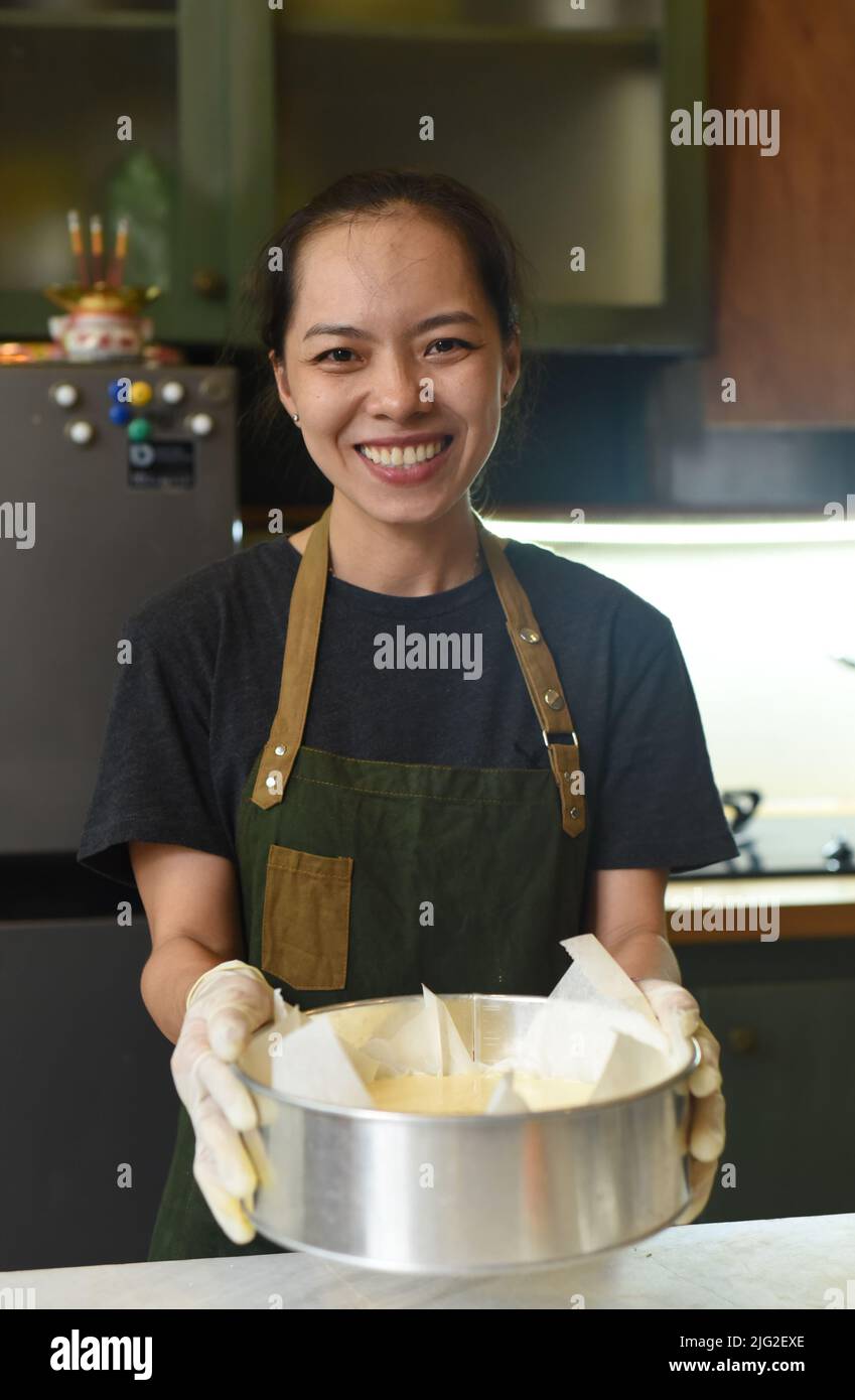 Donna vietnamita che tiene un piatto da forno con pasta di cheesecake in cucina Foto Stock