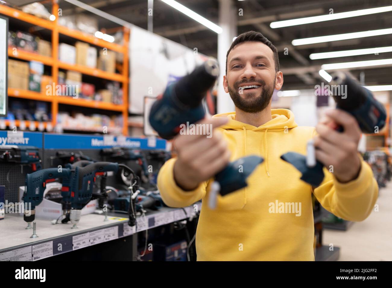 cliente soddisfatto in un negozio di hardware che tiene due cacciaviti cordless con un grande sorriso sul viso Foto Stock