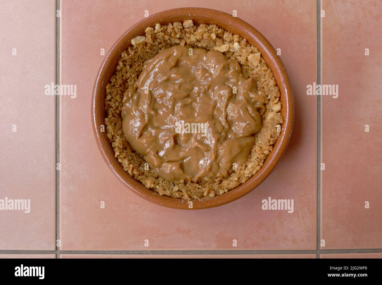 Una torta di banoffee delicioius nella preparazione, la base del biscotto è nel piatto insieme al caramello. Foto Stock