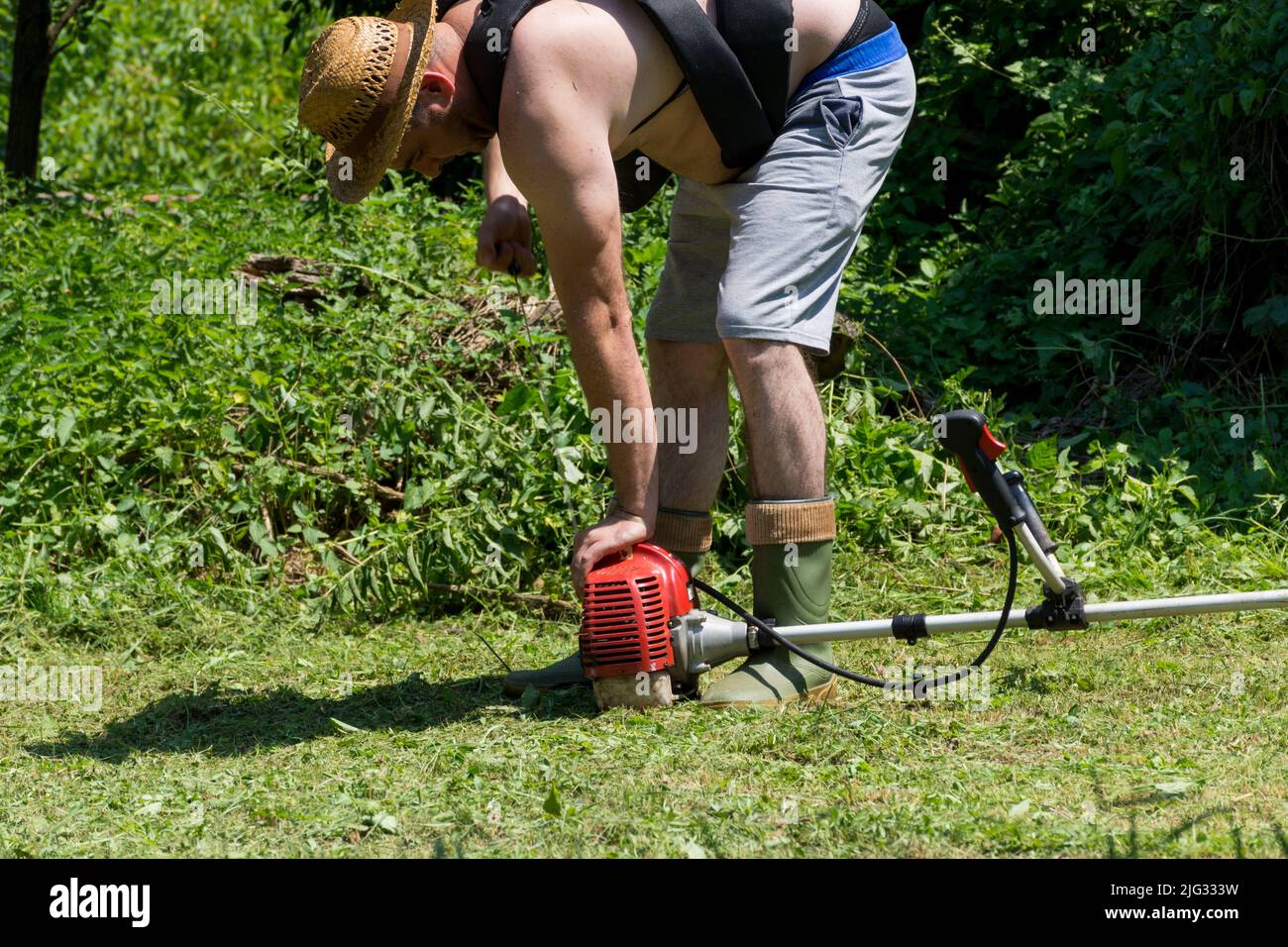 L'agricoltore ha iniziato un tosaerba manuale a benzina in un cortile in una giornata estiva soleggiata. Concetto di attrezzatura e strumento per il giardinaggio. Primo piano, messa a fuoco selettiva Foto Stock