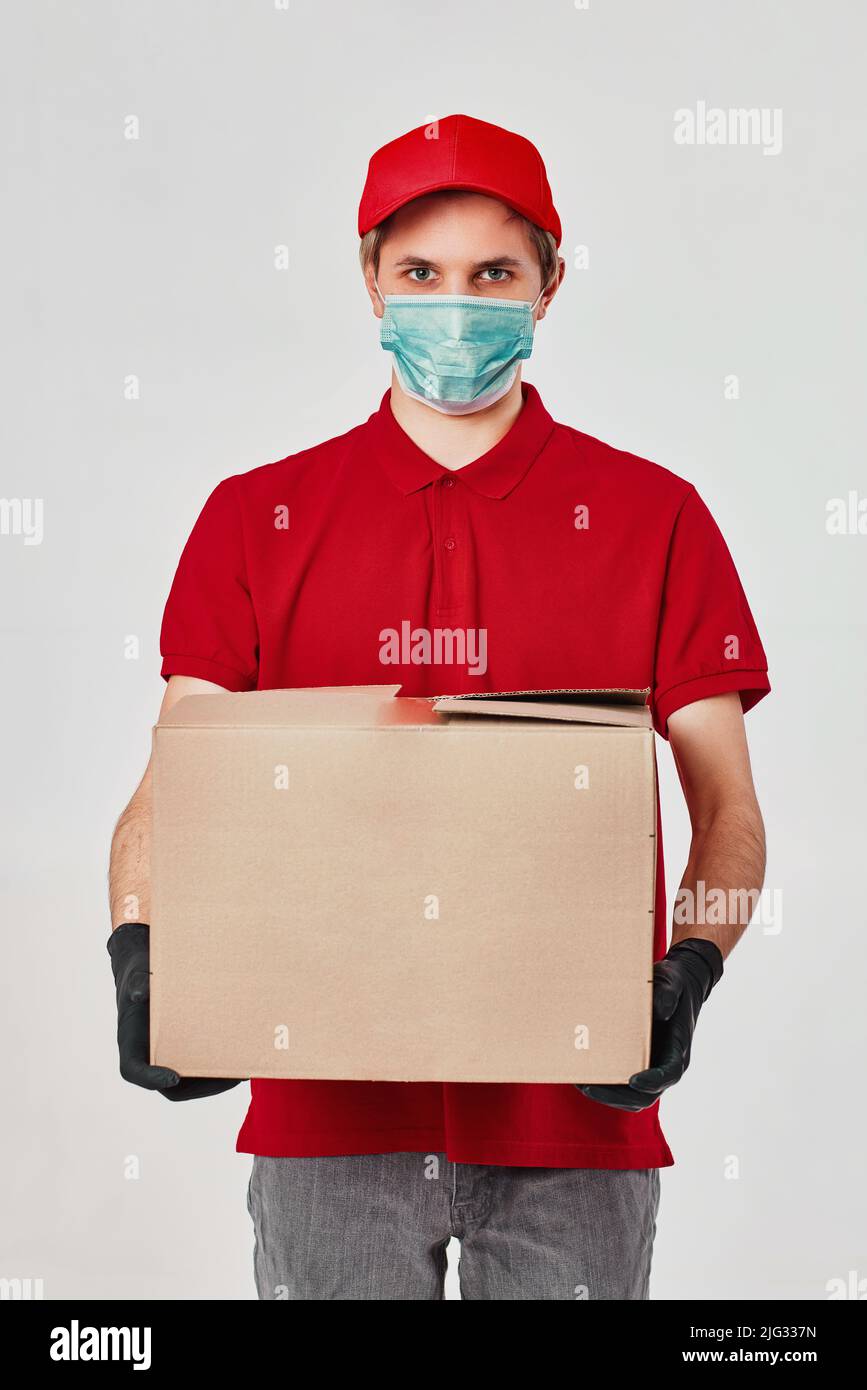 Addetto alla consegna in maschera con cappuccio rosso, scatola di cartone vuota Foto Stock