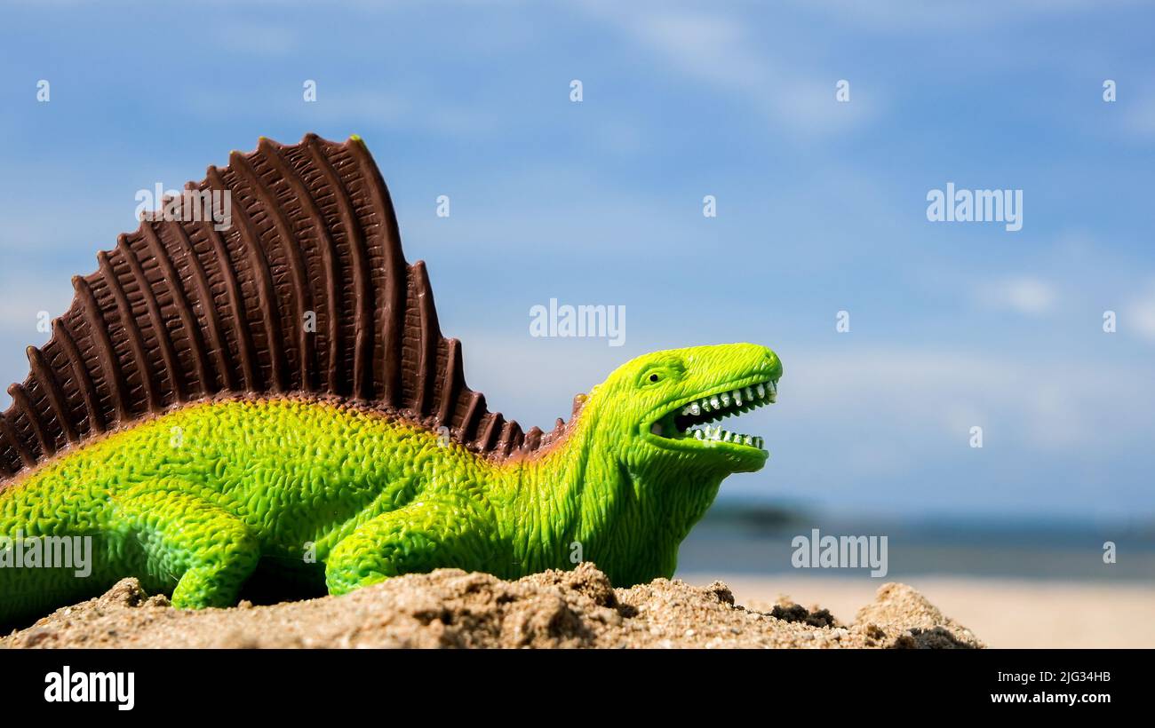 Dinosauro di plastica verde sulla spiaggia con cielo blu e spazio copia Foto Stock