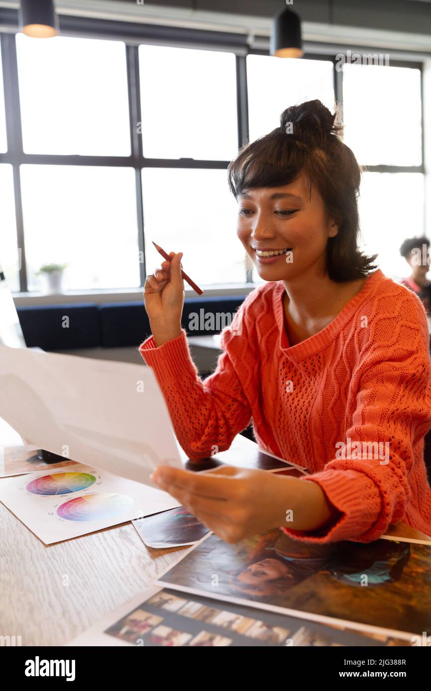 Sorridente giovane donna d'affari asiatica creativa con fotografia al banco in ufficio Foto Stock