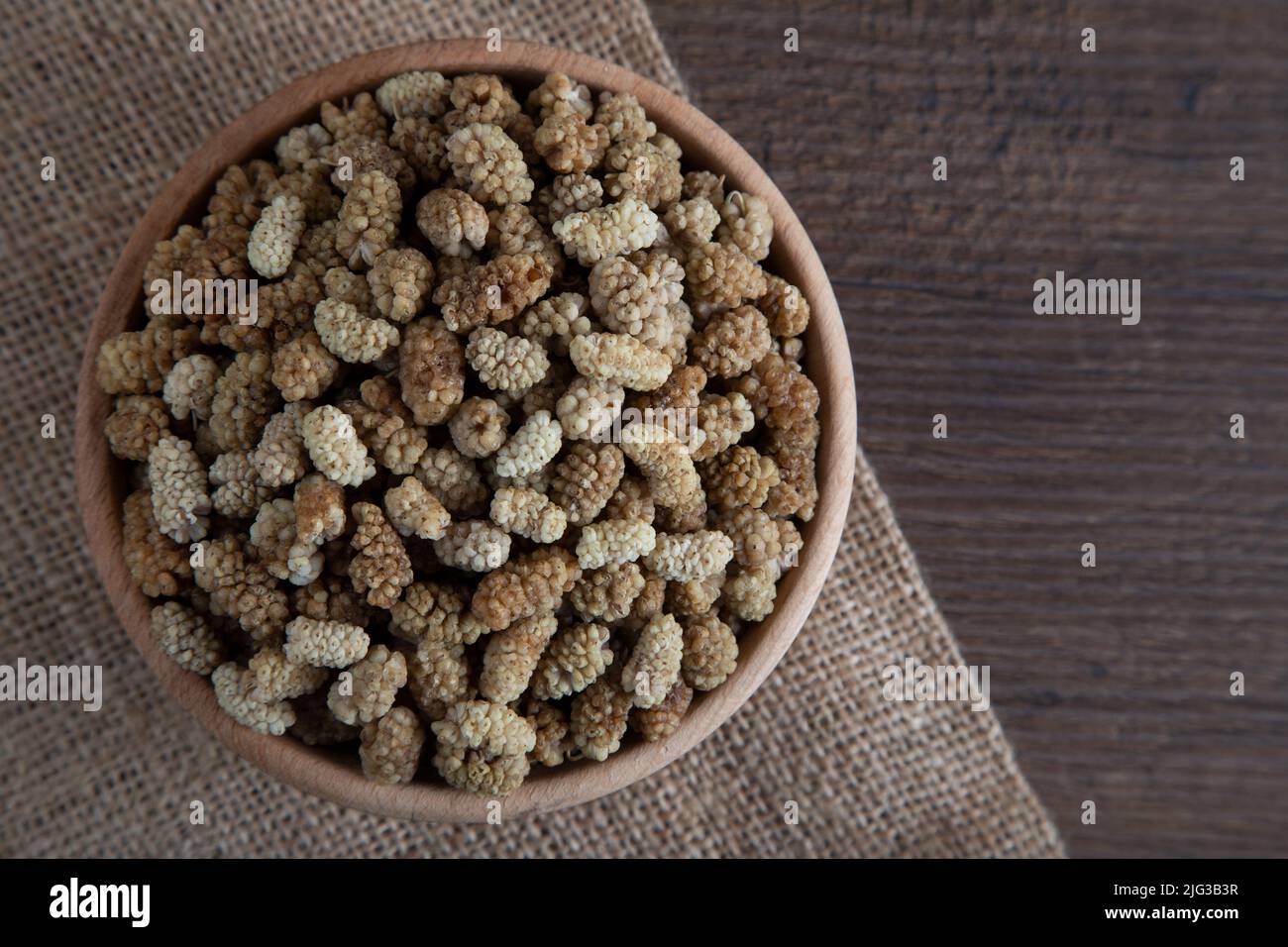 Ciotola piena di gelso secco su sfondo di legno Foto Stock