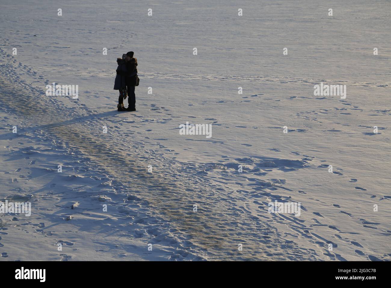 Due persone sole sul ghiaccio di un fiume ghiacciato, in un campo bianco di neve, abbracciati l'un l'altro Foto Stock