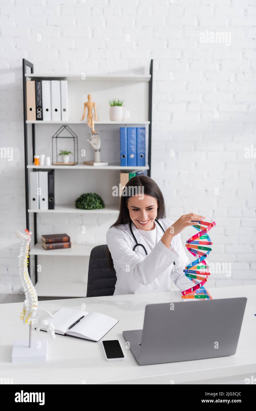 Medico positivo che tiene il modello di dna durante la video chat sul portatile in ospedale Foto Stock