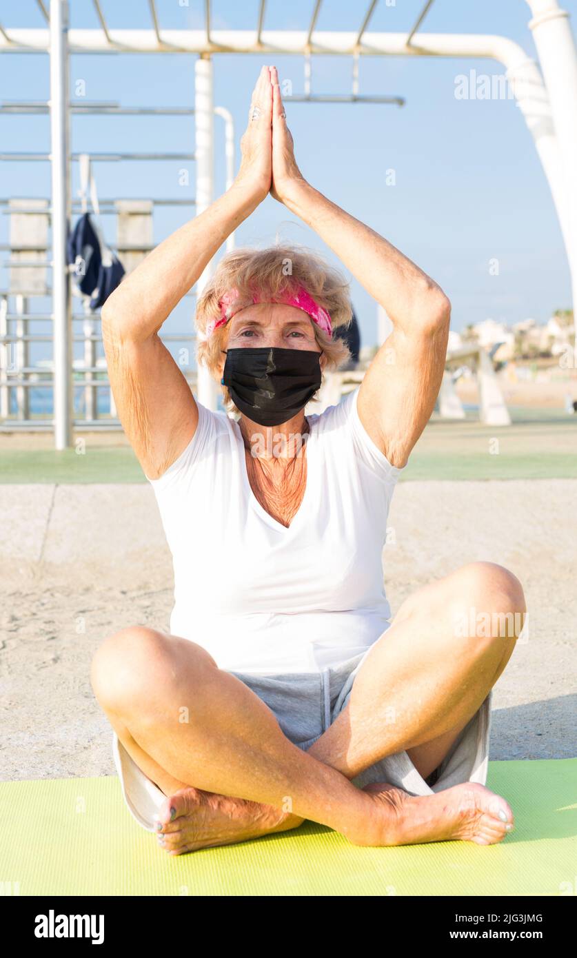 Vecchia signora in maschera in posa di loto all'aperto Foto Stock