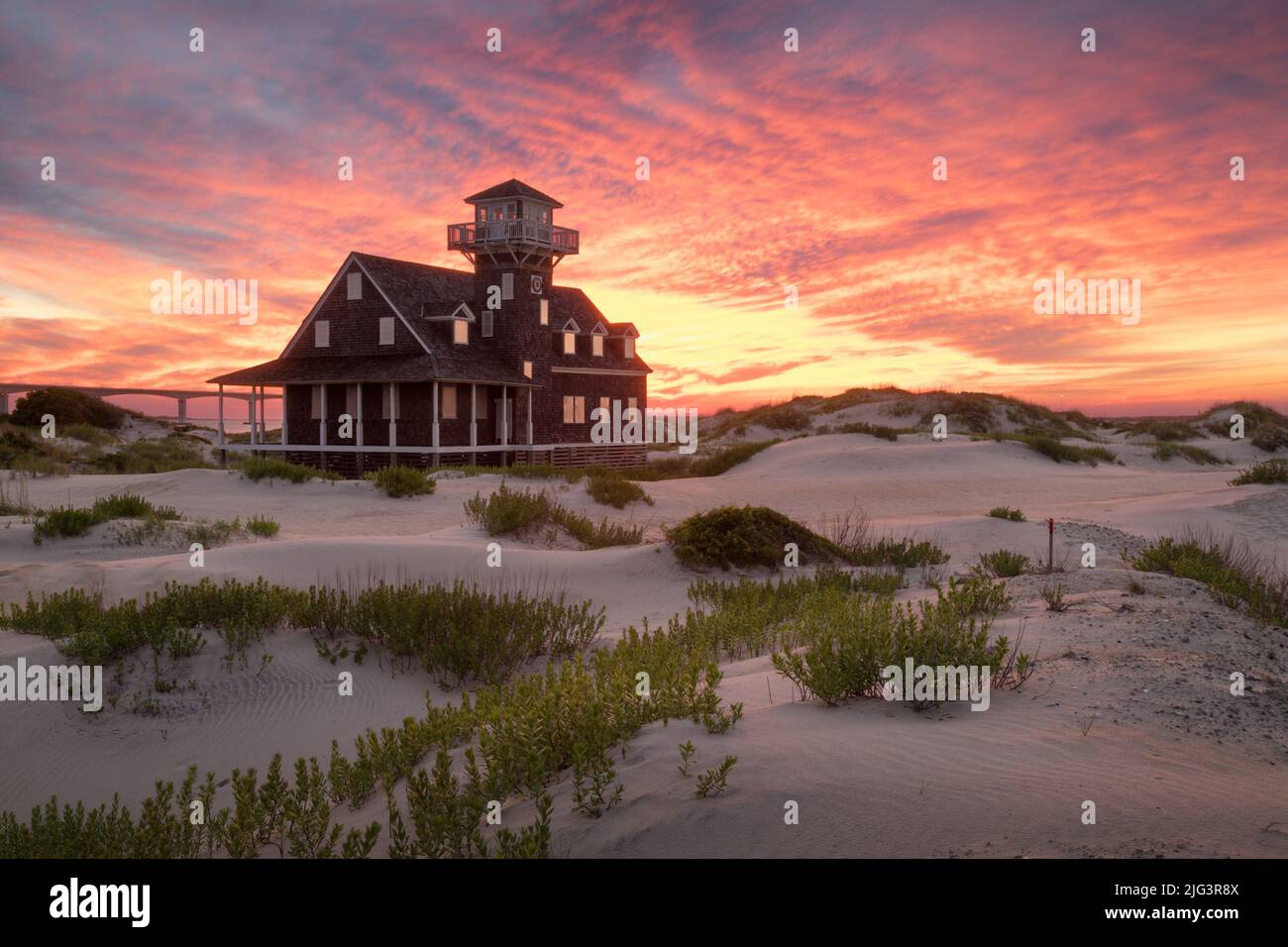 Oregon Inlet Lifesaving Station circondato da dune di sabbia sotto un tramonto giallo, viola e arancione nelle Outer Banks, North Carolina Foto Stock