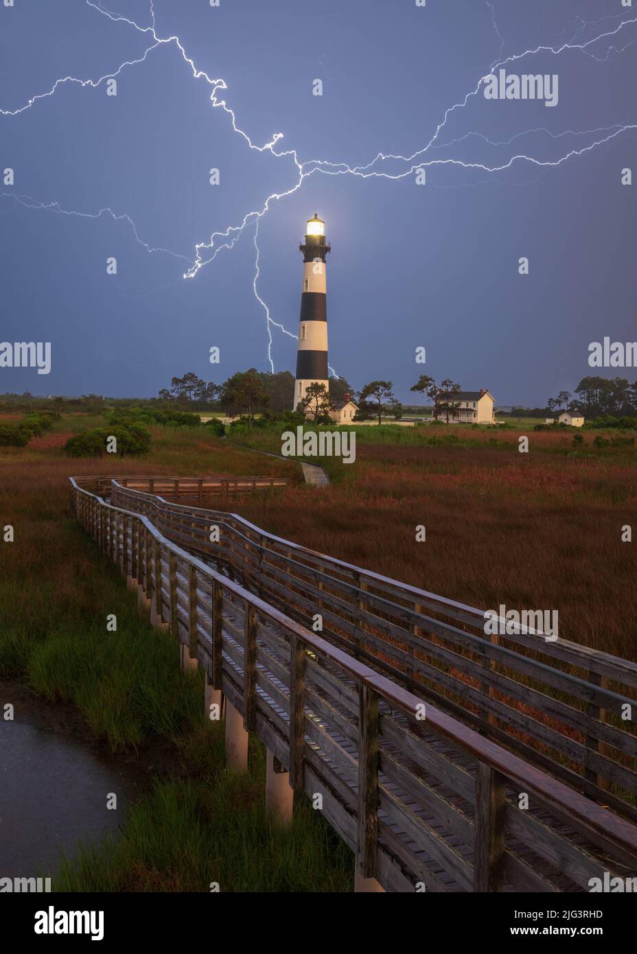 Passerella che conduce al faro di Bodie Island con fulmine in background in pioggia di notte, Outer Banks, North Carolina Foto Stock