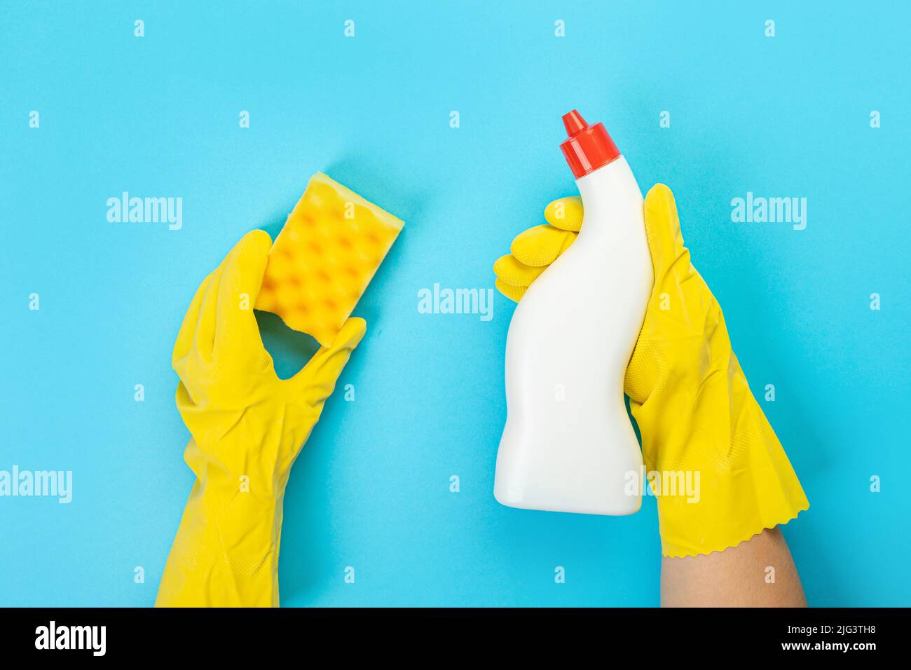 Le mani di una casalinga in guanti protettivi di gomma gialli tengono una bottiglia di prodotti chimici domestici e uno straccio. Detergente per varie superfici nel kitc Foto Stock