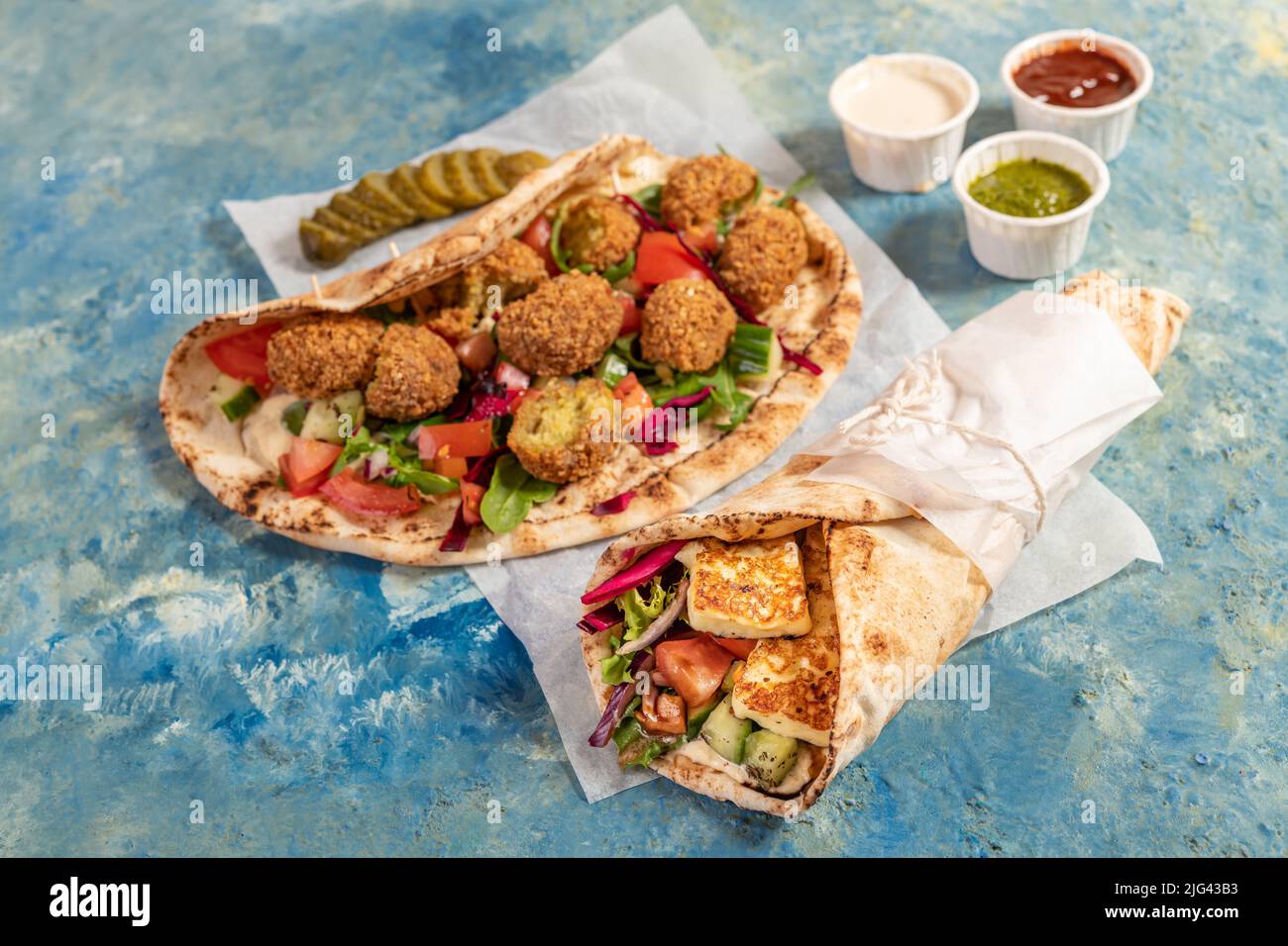 Tradizionali halloumi arabi alla griglia mediterranei e falafel, hummus e verdure in involtini di pane piatto con erbe e una varietà di salse Foto Stock