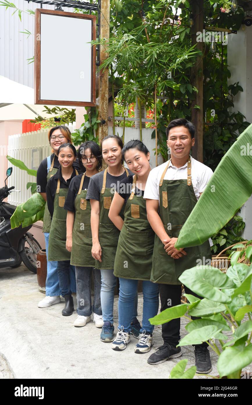 Il personale della caffetteria vietnamita sorride e si alza insieme contro un caffè Foto Stock
