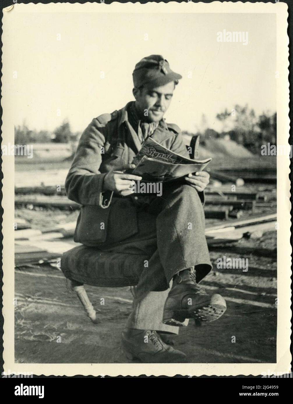 Ritratto del soldato divisionale che legge il segnale illustrato della rivista. Ritratto visionario con una uniforme tedesca e toccato con una berretto in un anca in una sedia rivestita mentre si legge la rivista di segnale illustrato a cura della casa editrice tedesca Deutscher Verlag, Signal è stato un supporto propagandistico della Germania nazista durante la seconda guerra mondiale Foto Stock