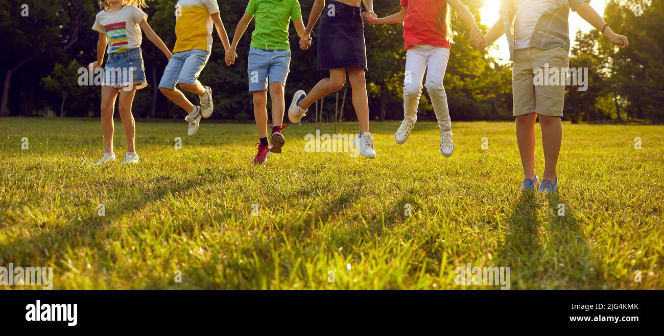 Ragazzi e ragazze felici che giocano insieme, divertirsi e saltare sull'erba verde nel parco Foto Stock