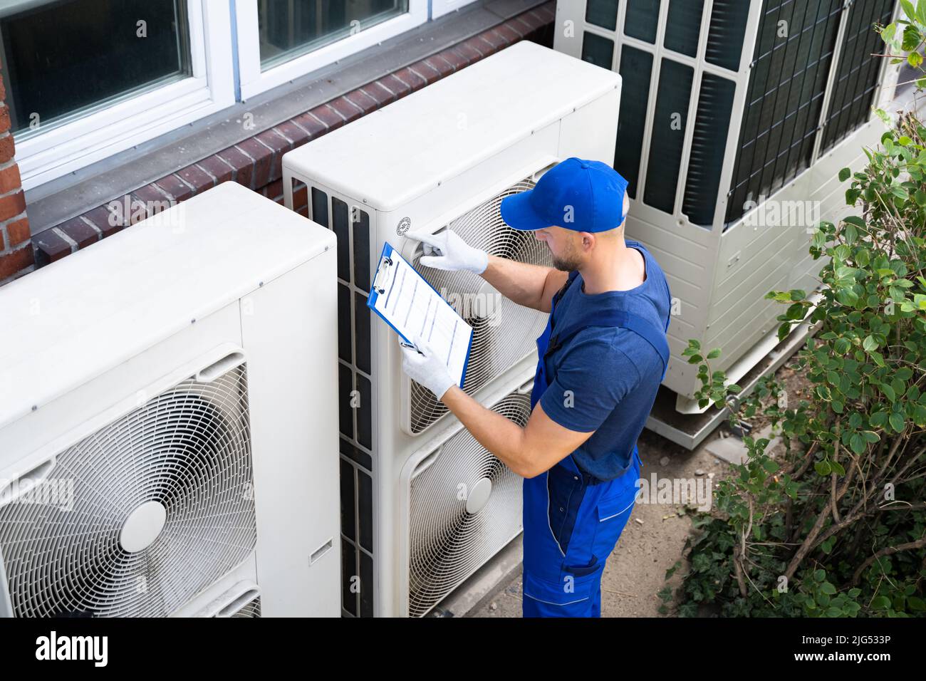 Elettricisti due uomini che indossano giacche di sicurezza Controllo unità aria condizionata sulla costruzione tetto Foto Stock