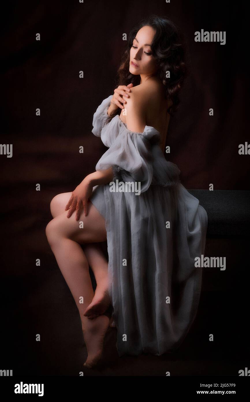 Bella donna latina in un vestito antico, lei sta posando seduta è molto confortevole, con sfondo nero, fotografia a basso tasto con luce spot. Foto Stock