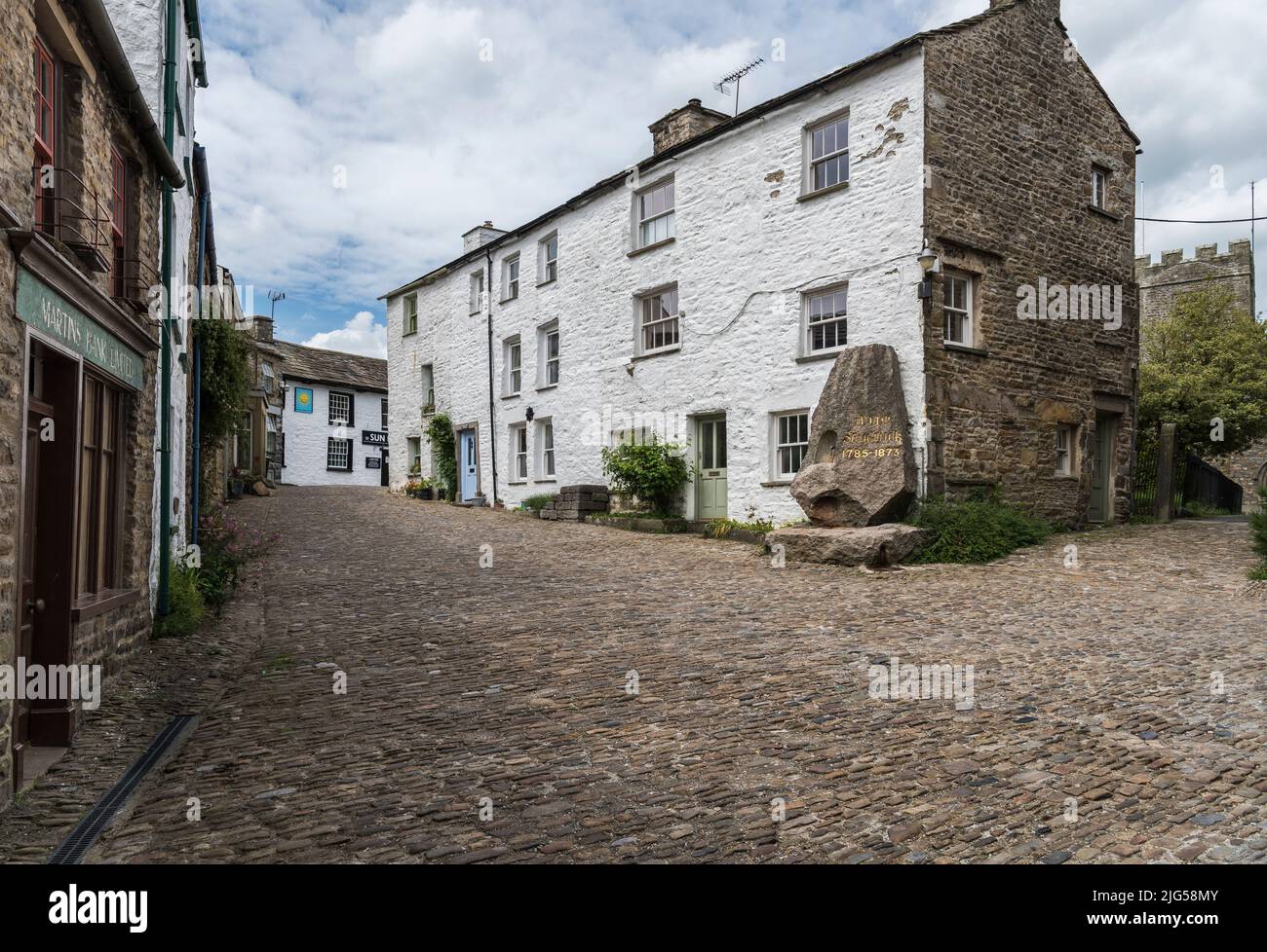 Edifici e strade acciottolate vuote nel centro del villaggio di Yorkshire Dales con memoriale di Adam Sedgwick e torre della chiesa castellata sullo sfondo. Foto Stock