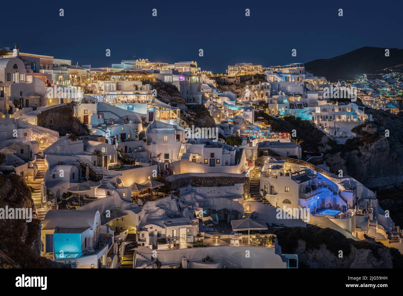 Vista panoramica di notte del villaggio di Oia a Santorini, con le sue case tipiche che ospitano suite e boutique hotel illuminati Foto Stock