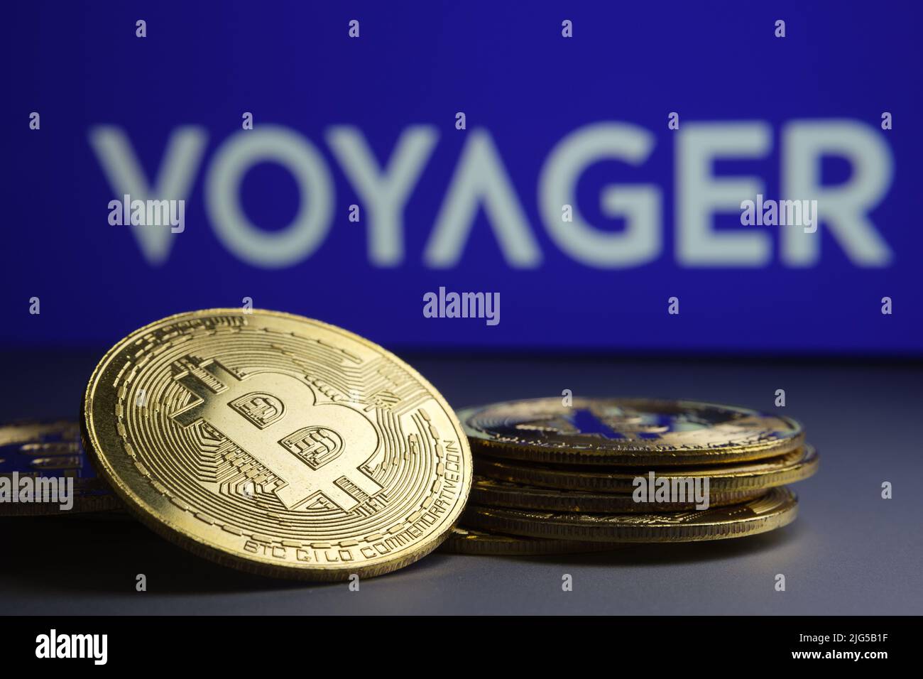 Pila caduta di gettoni Bitcoin e blurred il logo della società Voyager Digital Ltd su sfondo sfocato. Concetto di fallimento. Stafford, Regno Unito Foto Stock