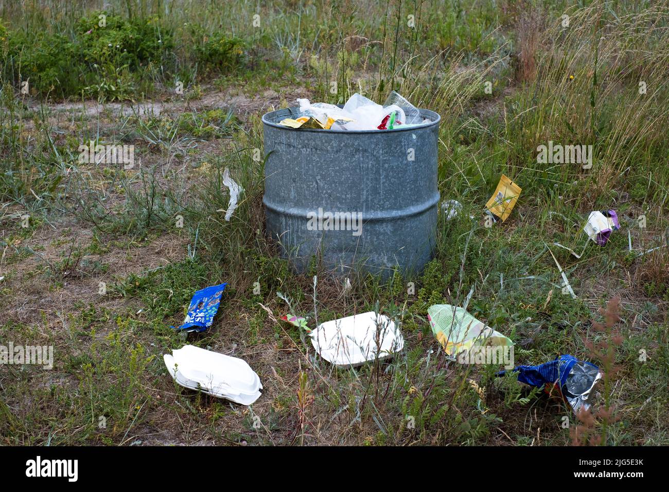 I rifiuti riempiti possono su un prato durante la giornata estiva di sole. Cestino in natura. Foto Stock