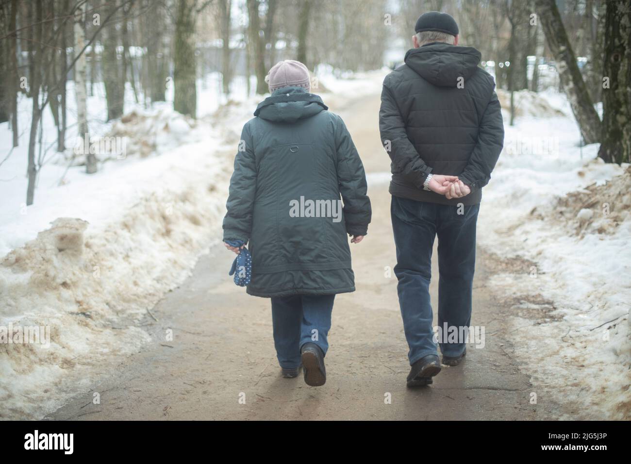 Uomo e donna camminano attraverso il parco in inverno. Persone in strada. Passeggia per la città. Persone anziane da dietro. Foto Stock