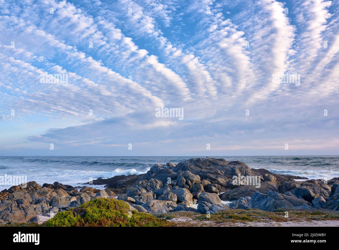 CopySpace in mare con un cielo blu nuvoloso sfondo e costa rocciosa nel Capo Sud Africa occidentale. Onde oceaniche e massi in una spiaggia vuota. Tranquillo Foto Stock