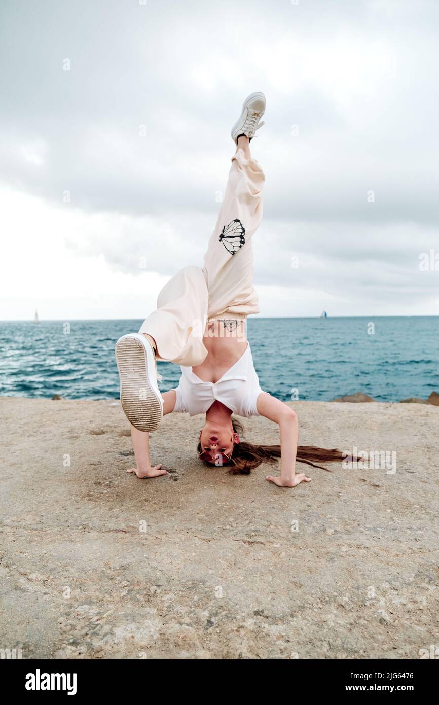 Danzatrice di breakdance che fa un cavalletto all'aperto vicino al mare. Foto Stock