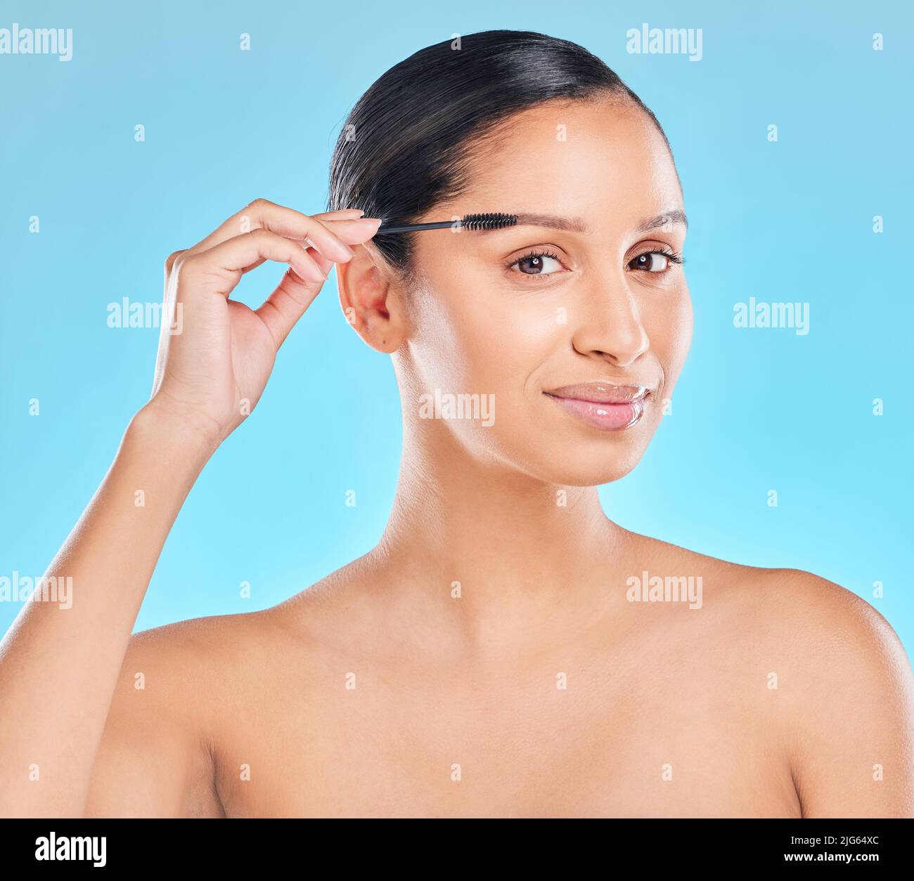 Non trascurate mai le vostre sopracciglia. Studio ritratto di una giovane donna attraente applicazione sopracciglia ombra su uno sfondo blu. Foto Stock