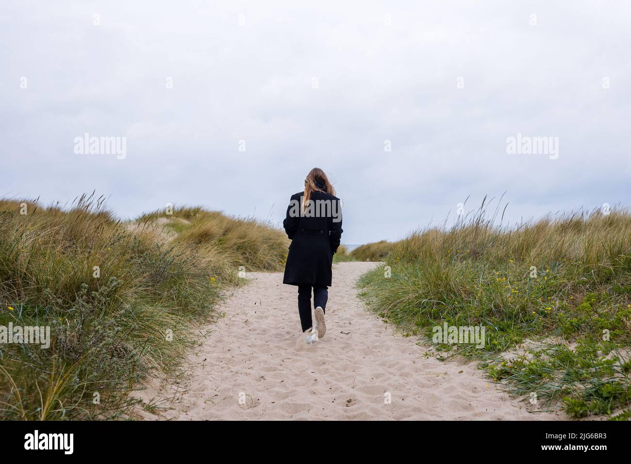 Donna con lunghi capelli che cammina sulla sabbia su un sentiero nelle dune vicino alla spiaggia Foto Stock