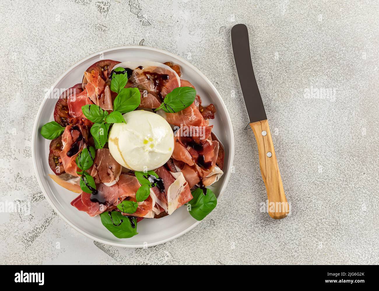 Prosciutto italiano con burrata, basilico fresco, pomodori e aceto balsamico. Superficie piana. Foto Stock