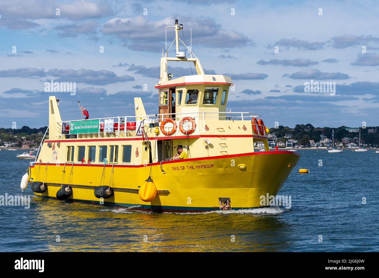 Barca gialla che si avvicina a Brownsea Island, Poole Harbour, Dorset, Inghilterra, Regno Unito, in un pomeriggio di sole per raccogliere i passeggeri Foto Stock