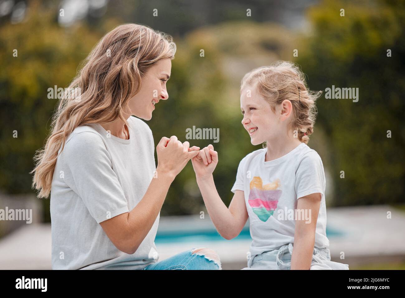 Felice giovane madre caucasica seduta con la sua adorabile bambina in giardino a casa e facendo le promesse pinky. Ragazza piccola carina che si lega con Foto Stock