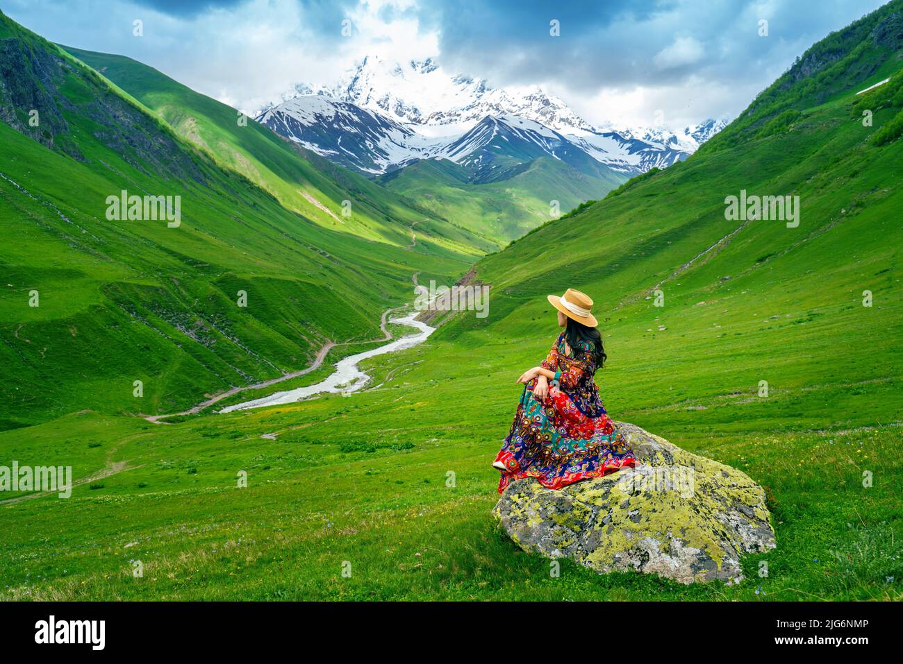 Turista seduto sulla roccia a pascolo verde contro la più alta montagna georgiana Shkhara vicino Ushguli in Georgia. Foto Stock