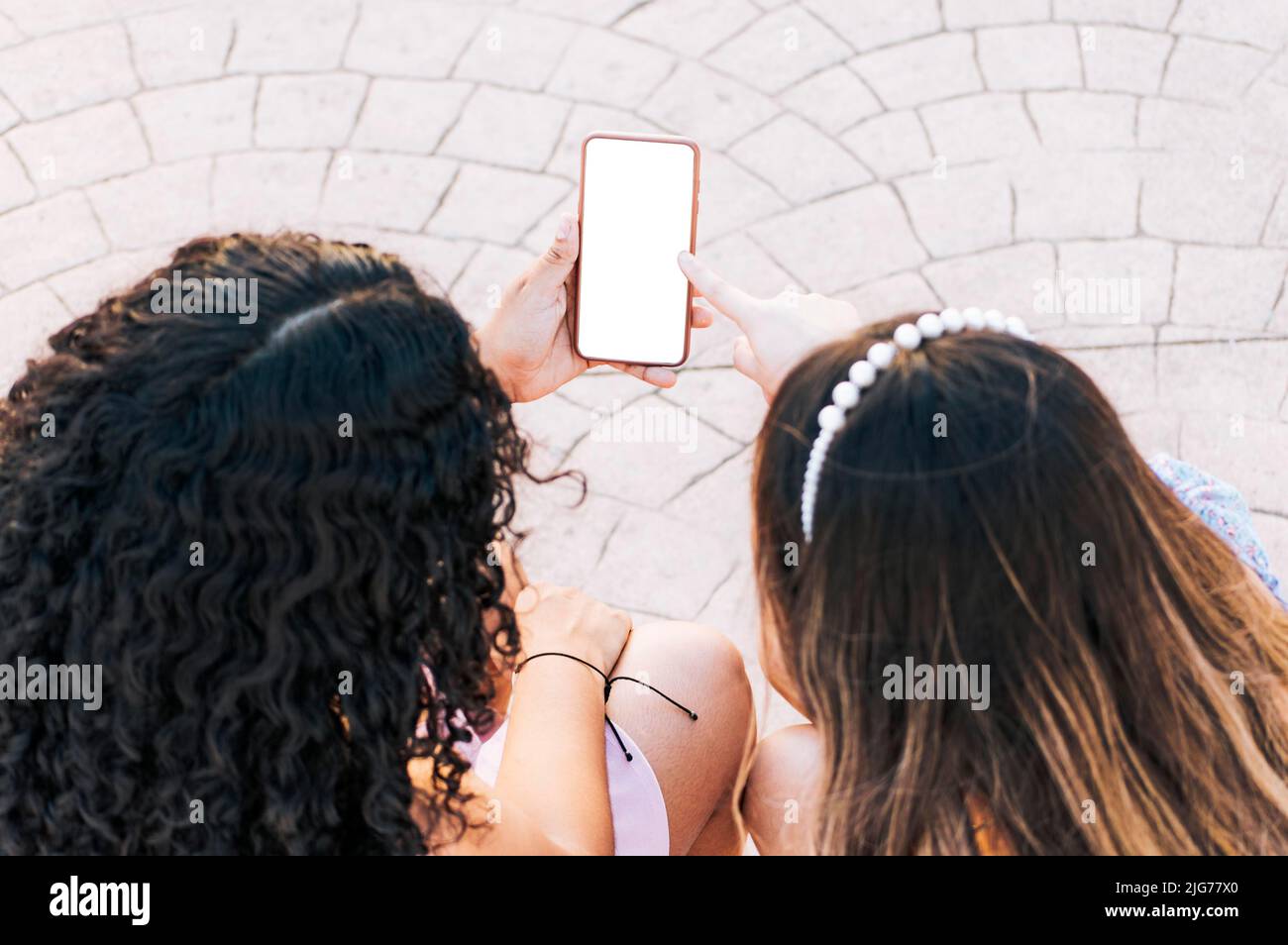 Mani di due ragazze che puntano allo schermo del telefono delle cellule, due ragazze che si siedono che puntano allo schermo del telefono delle cellule vuoto con lo spazio per il testo Foto Stock