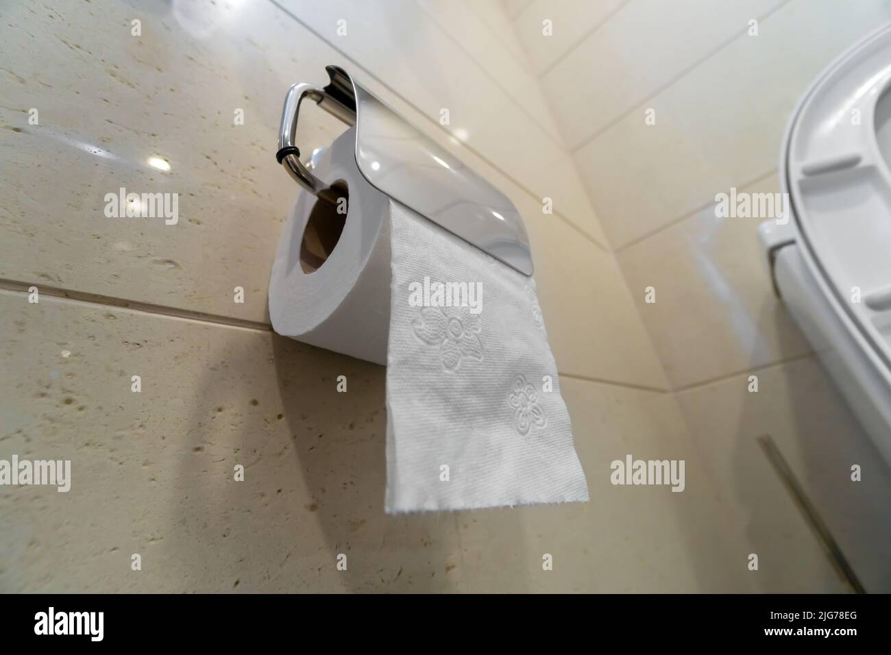 Primo piano di un rotolo di carta igienica appeso a una parete luminosa nella toilette, messa a fuoco selettiva Foto Stock