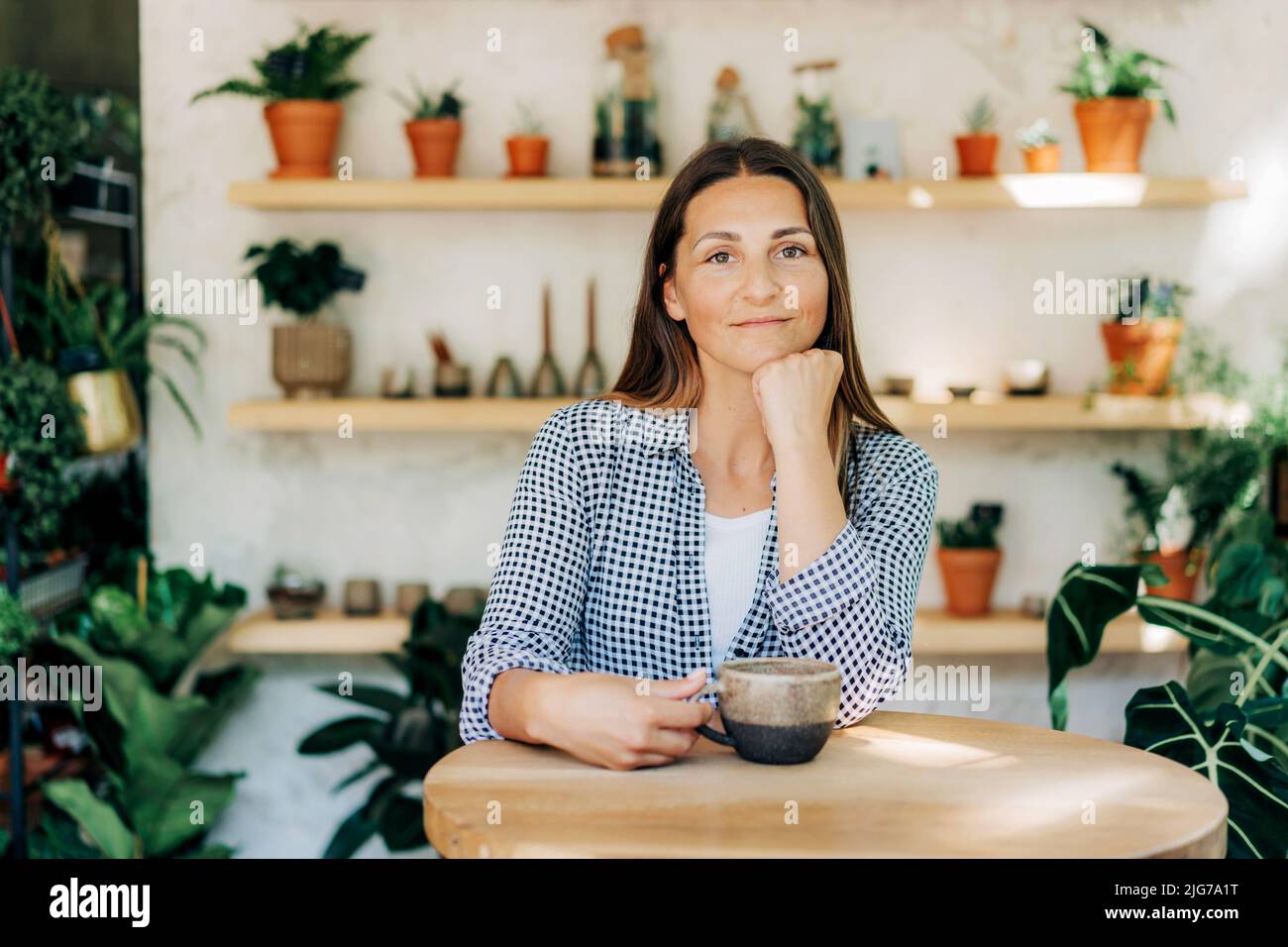 Bella donna brunetta 40s al bar in un negozio accogliente con piante Foto Stock