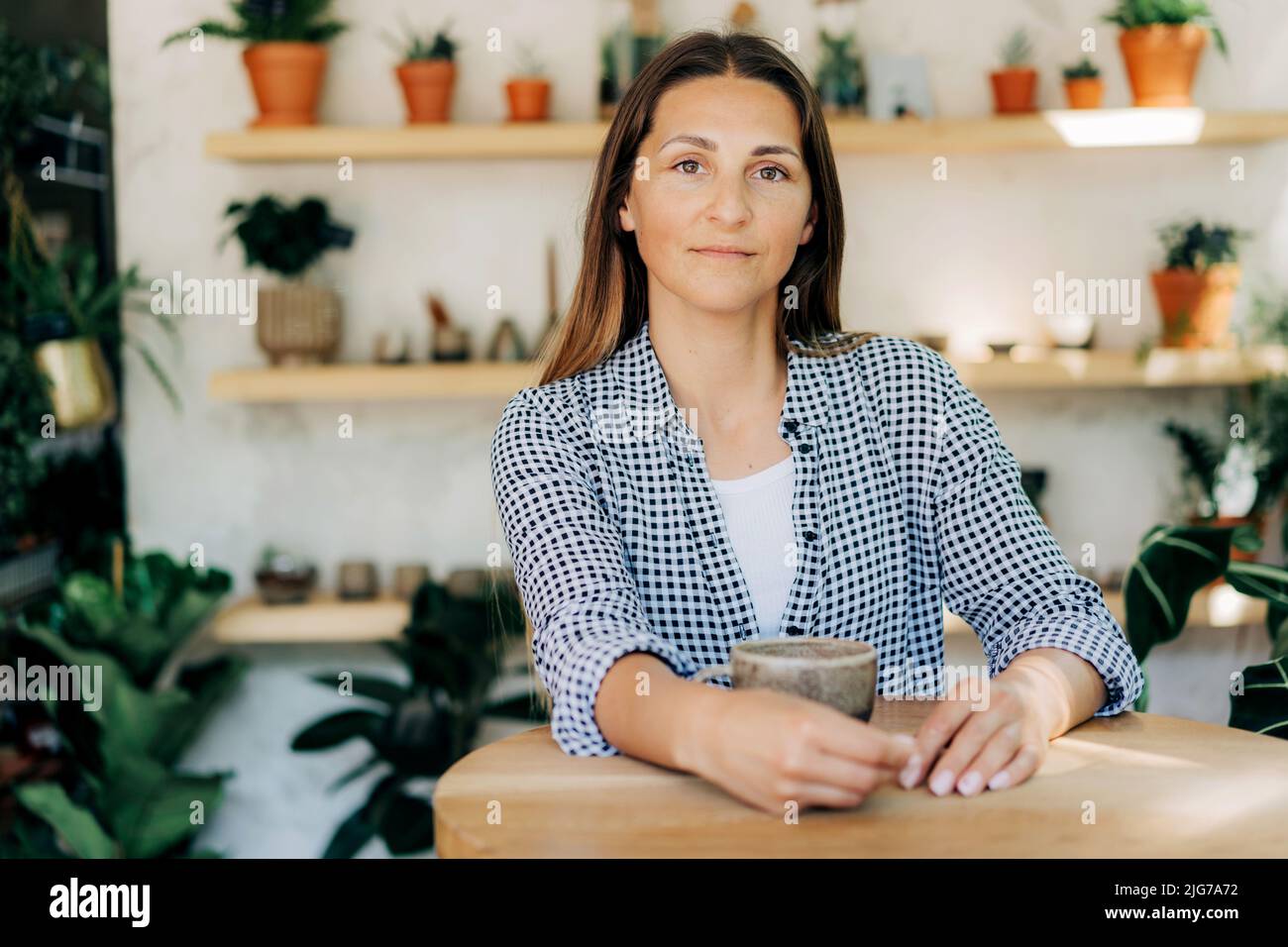 Bella donna brunetta 40s al bar in un negozio accogliente con piante Foto Stock