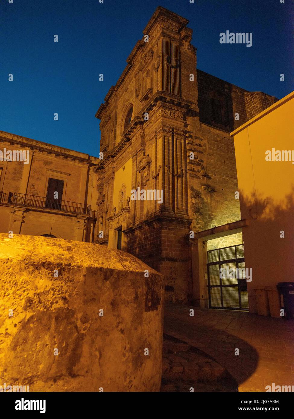 Una chiesa abbandonata con una facciata ornata ma oscurata riflessa dalle luci di strada nelle strade posteriori di Nardo, Puglia al tramonto. Foto Stock