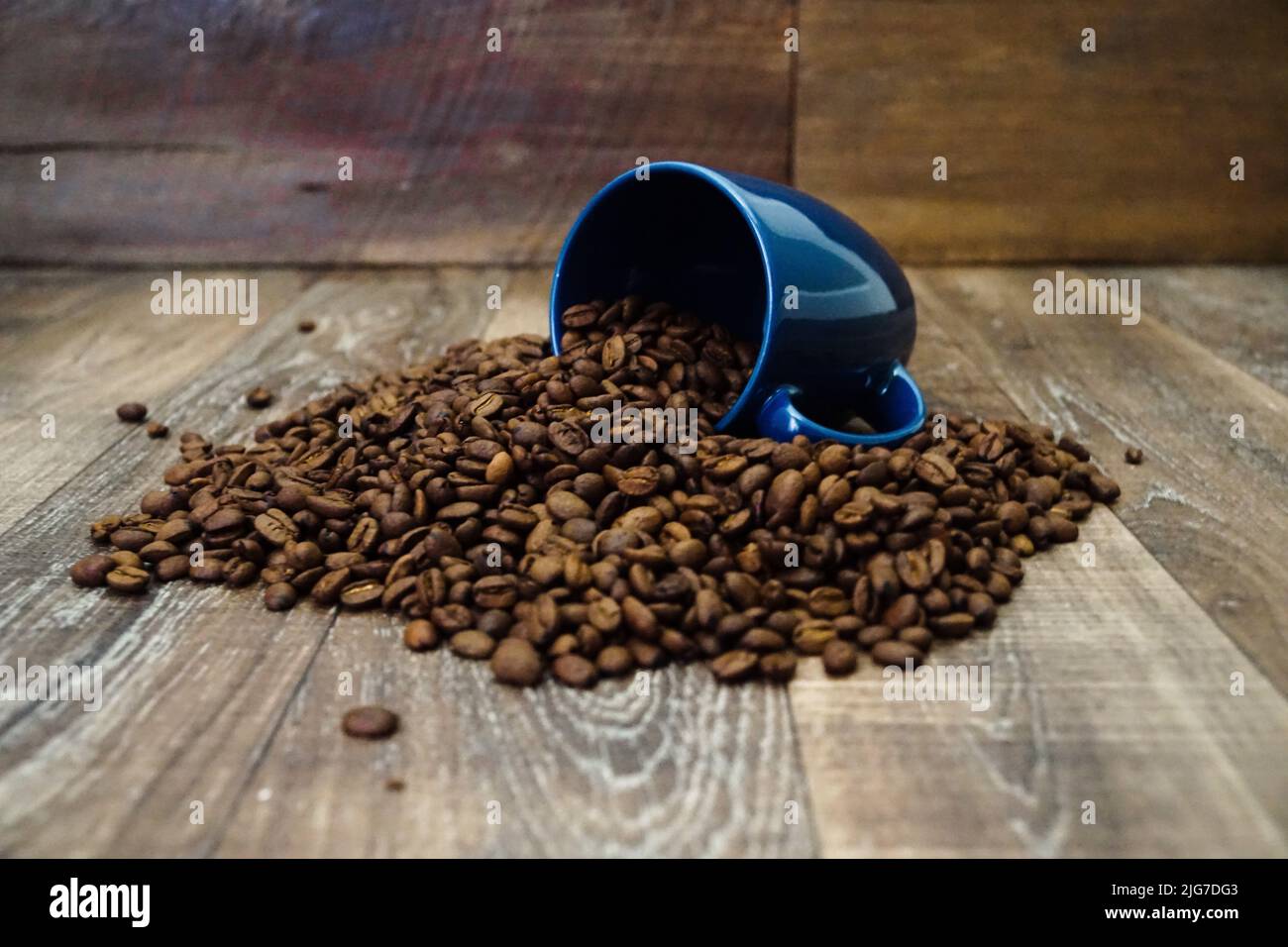 Una tazza di caffè blu viene capovolta con i chicchi che fuoriescono dalla tazza su una superficie di legno. Foto Stock