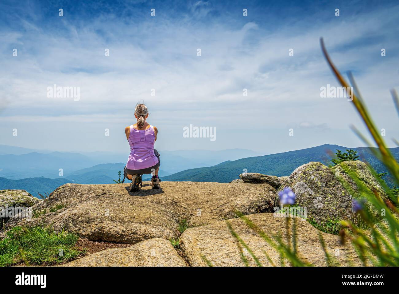 Vista posteriore di una donna escursionista che squatting su una roccia fuori che mozzano nelle Blue Ridge Mountains in una giornata di sole. Foto Stock