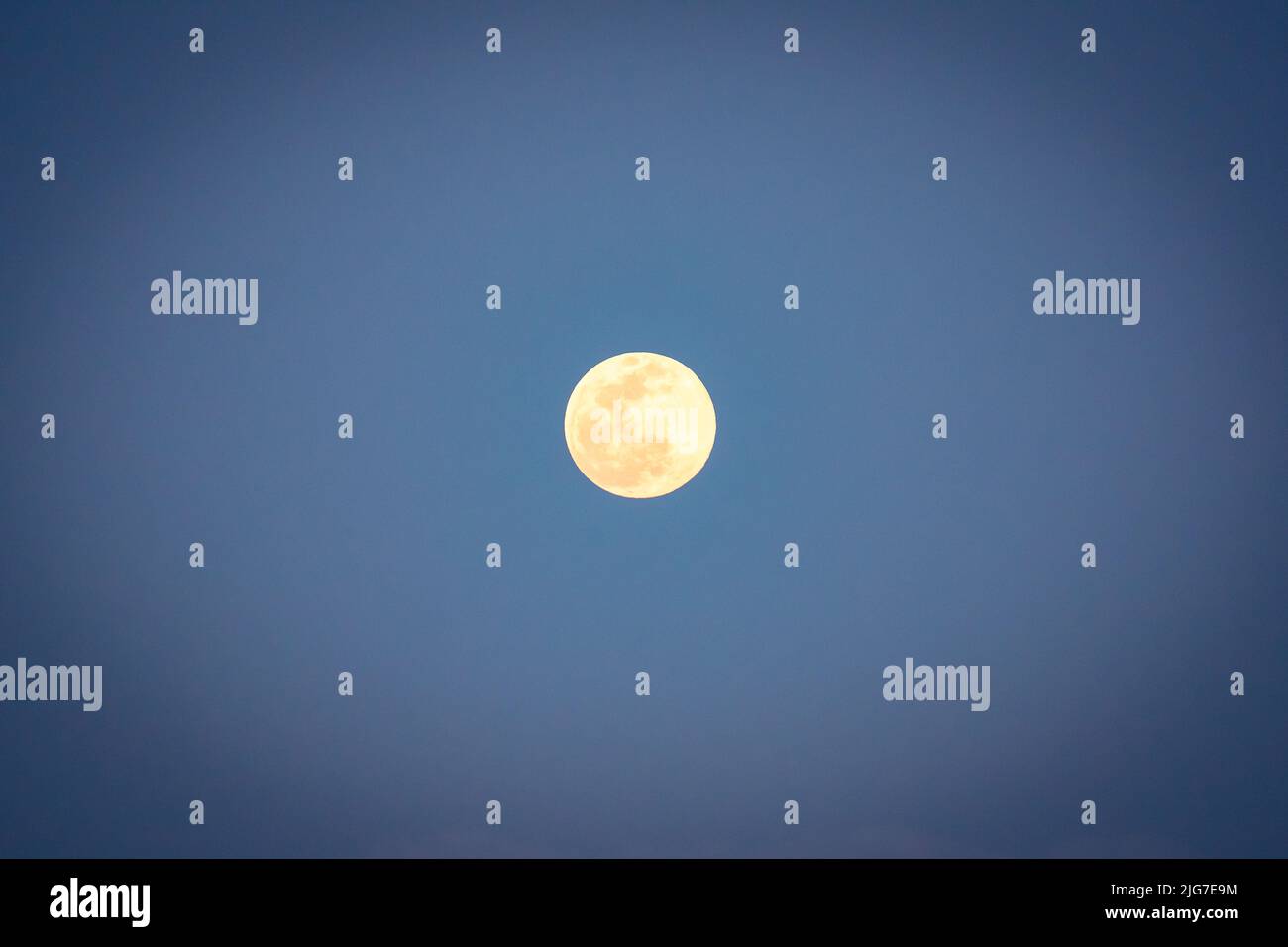 La luna piena si illumina di dettagli contro un cielo blu chiaro Foto Stock