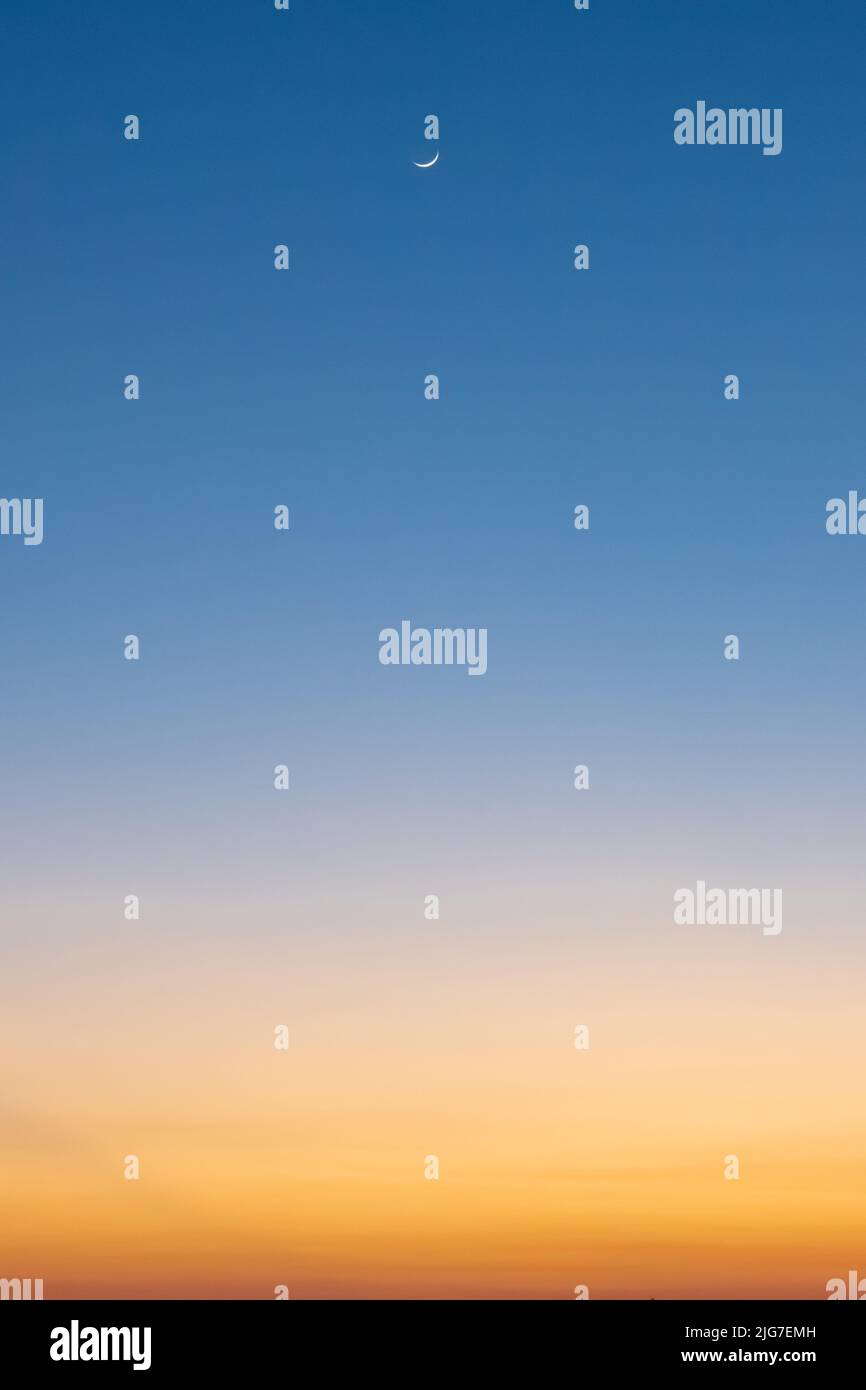 Il nastro di luna è alto in un cielo di tramonto dai colori brillanti. Foto Stock