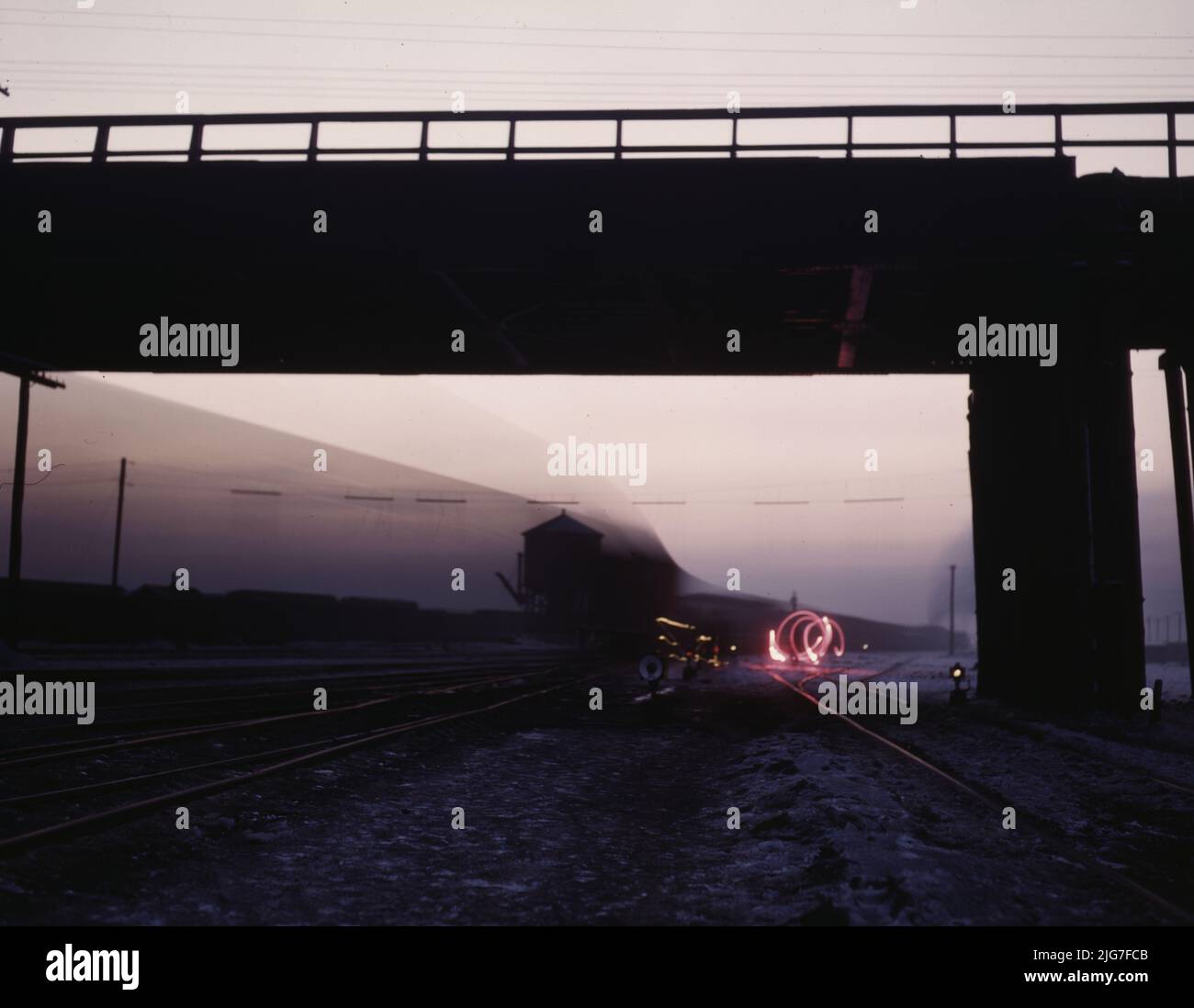 Visualizza in un cantiere di partenza a C&amp; NW RR [es Chicago e North Western Railroad's] Proviso (?) Iarda al crepuscolo, Chicago, Ill. Brakeman sta segnalando con un fuoco rosso e il treno sta andando vicino durante l'esposizione. Foto Stock