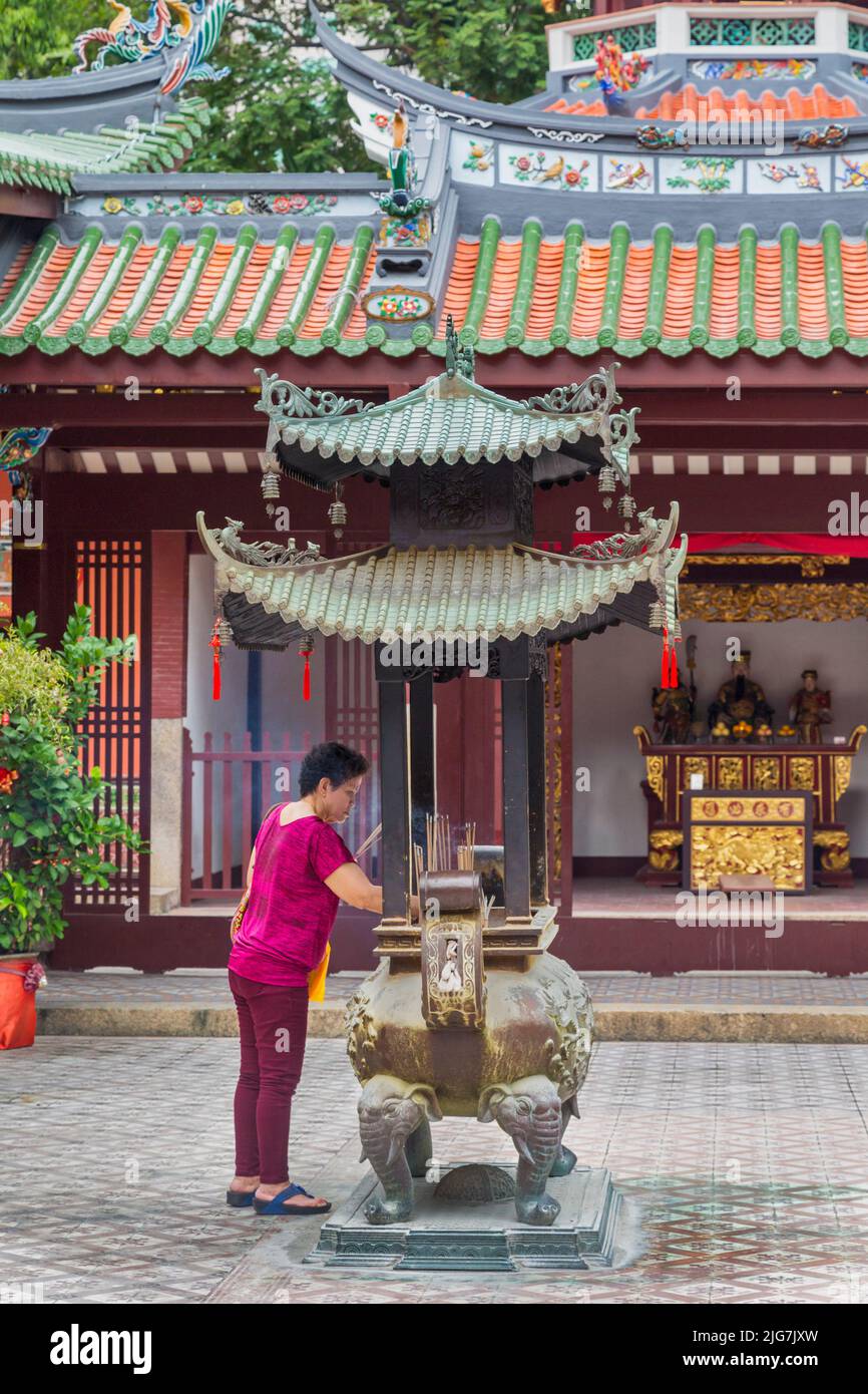 Una donna illumina un bastone di scherzo nei cortili del tempio Thian Hock Keng, o Tempio della felicità celeste, Singapore. Il tempio risale al 1839 A. Foto Stock