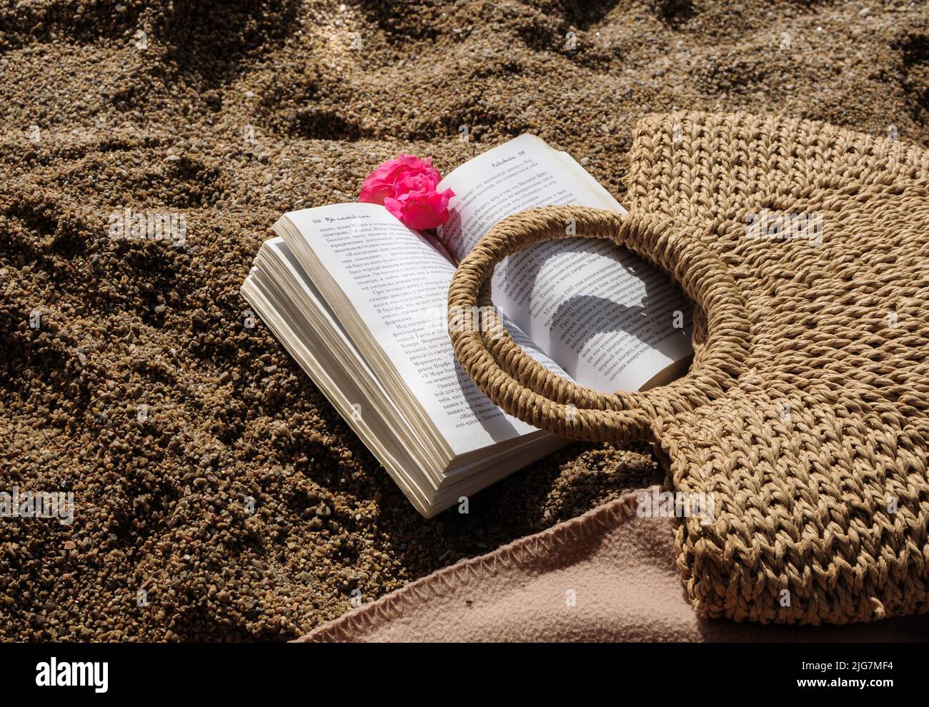 Vista dall'alto degli accessori da spiaggia: Borsa in maglia di paglia e un libro su una spiaggia sabbiosa Foto Stock