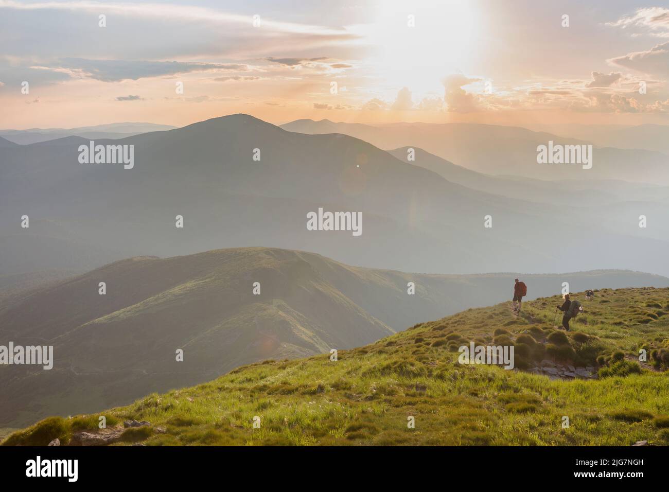 Due escursionisti turistici nelle colline lapidate delle montagne durante il tramonto con il cielo arancione e le nuvole nei Carpazi, Chornohora, Petros Foto Stock